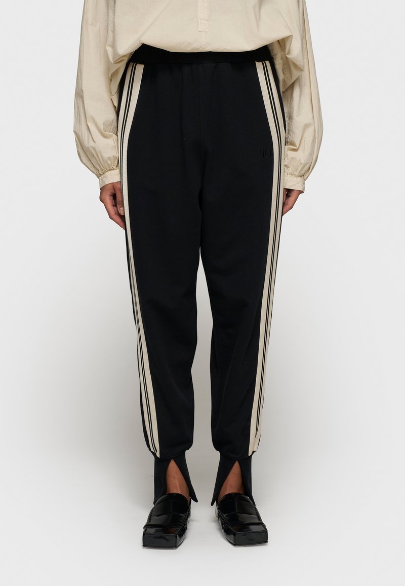 Zwarte joggingsbroek met beige zijstrepen, tapered fit, elastische tailleband en open splitten aan de onderkant. Gemaakt van een katoenmix.