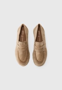 Mocassins en daim beige avec un bout rond cousu et une bande décorative sur le cou-de-pied. Semelle texturée et rembourrée pour un confort optimal.