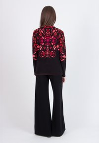Black sweater featuring a vibrant floral design in red and pink hues, paired with wide-leg black pants. Smooth texture, relaxed fit.