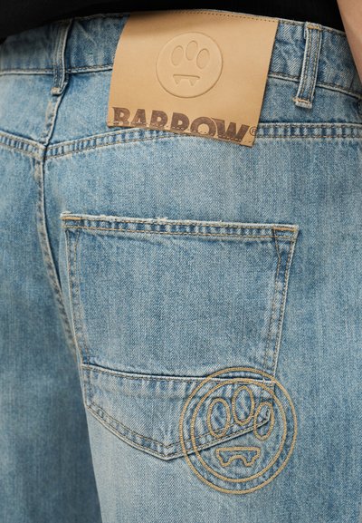 Φωτεινό μπλε τζιν με σχεδιασμό κυκλικού προσώπου κεντημένο στην πίσω τσέπη και ετικέτα από δέρμα σε καφέ απόχρωση με αποτύπωμα πατούσας και την επιγραφή "BARROW".