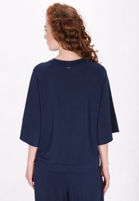 Maglietta blu navy, ampia e morbida, con maniche corte a tre quarti e scollo rotondo. Tessuto soffice e piccolo logo sulla schiena.