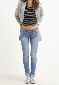 Gray long blazer over a black and white striped crop top, paired with light blue distressed skinny jeans and white sneakers.