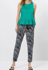 Haut en peplum sans manches turquoise associé à un pantalon à motifs paisley avec des accents teal, bordeaux et noir. Des sandales plates complètent la tenue.