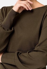 Olivengrüner Strickpullover mit weitem Ausschnitt, langen puffärmel und gerippten Bündchen, aus einem weichen, strukturierten Stoff.