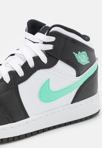 Středně vysoké tenisky s černým koženým svrškem a bílými akcenty. Mají mátově zelený Nike swoosh a logo Air Jordan. Texturovaná podrážka.