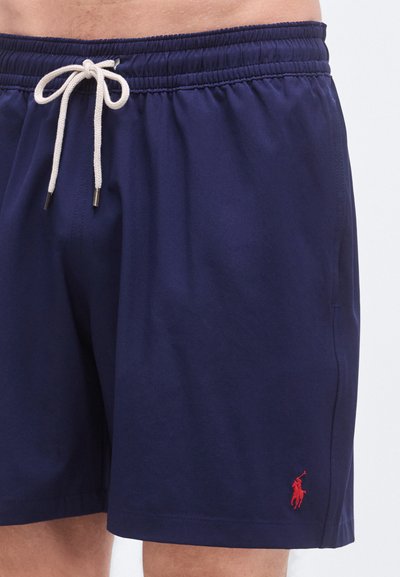Marineblå badeshorts i lett stoff med elastisk midjebånd, med snor og en liten rød logo på forsiden.