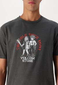 Donkergrijze katoenen t-shirt met een grafisch ontwerp van twee cartoonfiguren, een met stekels in het haar, en de tekst "Problemen sinds 1991."