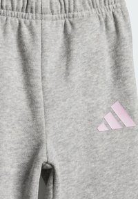 Pantalones de chándal grises hechos de un tejido suave, con cintura elástica y un logo de Adidas en rosa en la parte inferior de la pierna; diseño duradero y cómodo.