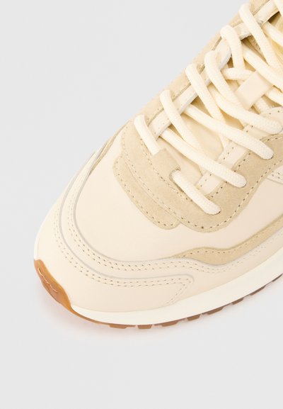 Beige Sneaker aus einer Kombination von glattem Leder und Wildleder, mit strukturierten Akzenten, hellbeigen Schnürsenkeln und einer hellbraunen Gummisohle.