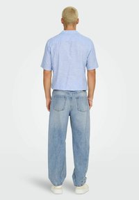 Ljust blå kortärmad skjorta, avslappnad passform, kombinerad med urtvättade, löst sittande denimjeans och vita sneakers. Bakview av outfiten.