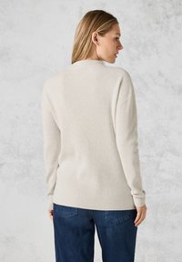 Heller beiger, gerippter Pullover mit langen Ärmeln, rundem Ausschnitt und lässiger Passform, kombiniert mit dunkelblauen Jeans.