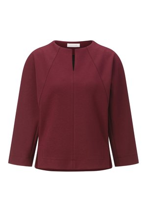 Top bordeaux con scollatura tonda, maniche a tre quarti, apertura a chiave frontale e tasche laterali. Tessuto liscio e texture con dettagli delle cuciture.