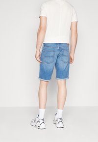 Pantalones cortos de mezclilla en azul claro, con dobladillo enrollado y bolsillos traseros. Combinados con una camiseta blanca y zapatillas deportivas blancas con acentos en azul marino.