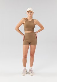 Ensemble composé d'un crop top côtelé marron et d'un short taille haute. Le tissu est texturé, s'ajustant parfaitement, associé à des baskets de couleur claire et une casquette blanche.