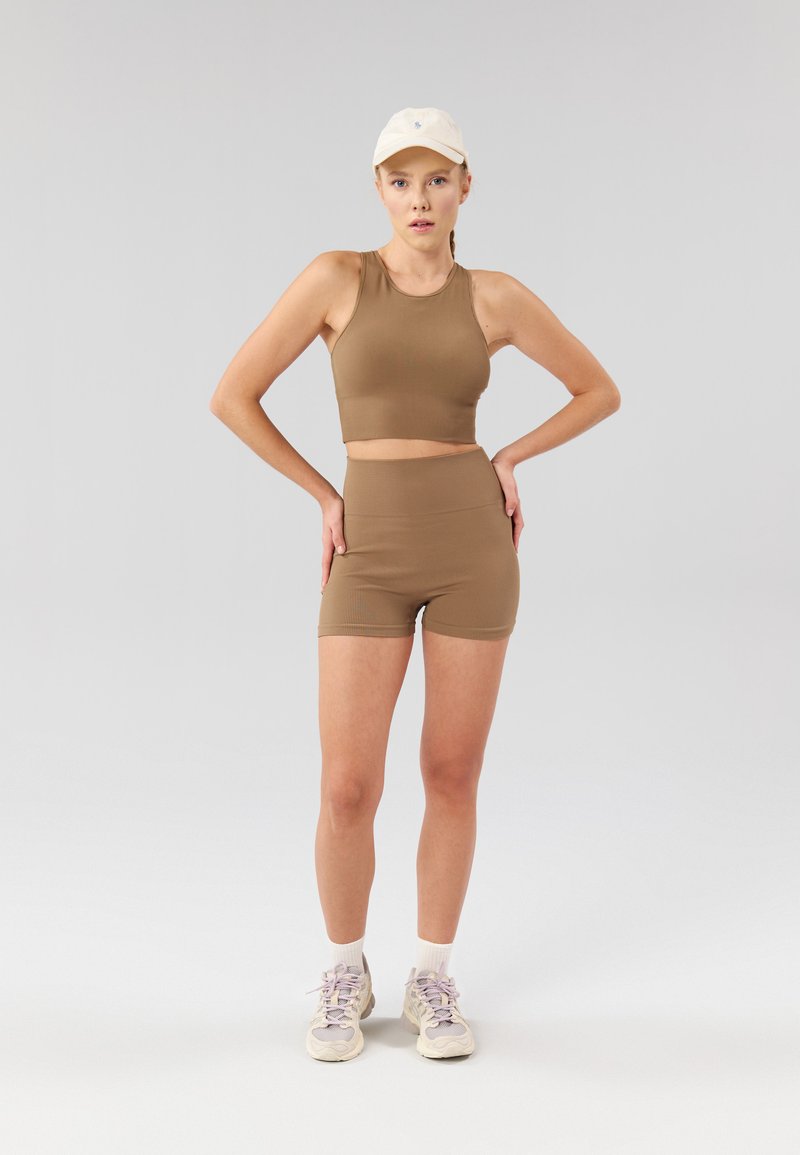 Ensemble composé d'un crop top côtelé marron et d'un short taille haute. Le tissu est texturé, s'ajustant parfaitement, associé à des baskets de couleur claire et une casquette blanche.