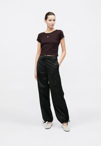 Camiseta corta burdeos con mangas cortas y logo, combinada con pantalones cargo negros holgados que cuentan con un bolsillo lateral y puños elásticos.