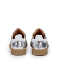 Chaussures en cuir argenté avec une finition texturée, des accents blancs et une semelle en caoutchouc beige arborant le nom de la marque "LLOYD" sur le talon.