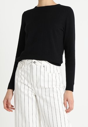 Haut noir à manches longues avec un col rond associé à un pantalon taille haute à rayures blanches doté de matériel argenté et d'une coupe ajustée.