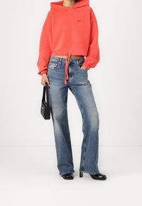 Sudadera recortada coral con cordones, combinada con vaqueros de pierna ancha azul claro. Bolso negro y tacones puntiagudos completan el conjunto.