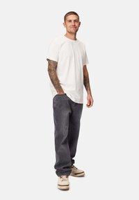 Hvid bomulds T-shirt, afslappet pasform, parret med mørkegrå denim bukser med løs pasform. Skoene er beige med brune accenter.
