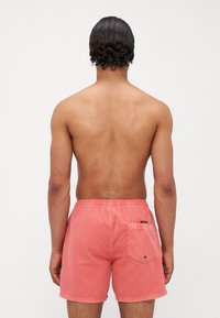 Koraļļu peldbikses, kas izgatavotas no viegla auduma, ar kabatu aizmugurē, elastīgu jostasvietu un gludu virsmu.