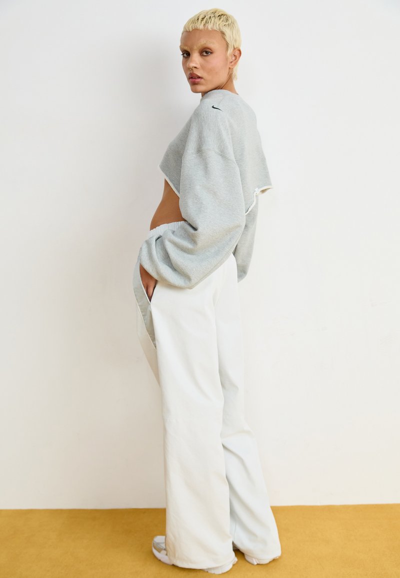 Grauer, kurz geschnittener Pullover mit weiten Ärmeln, kombiniert mit locker sitzenden weißen Hosen. Das Outfit zeichnet sich durch ein lässiges, entspanntes Design aus.