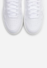 Paire de baskets blanches propres avec lacets, vues d'en haut, montrant des perforations sur la zone des orteils et une surface en cuir texturée.
