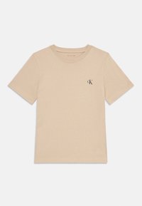 Tricou din bumbac bej, cu mâneci scurte, guler rotund și un mic logo CK gri închis pe partea stângă a pieptului. Textură netedă, design simplu.