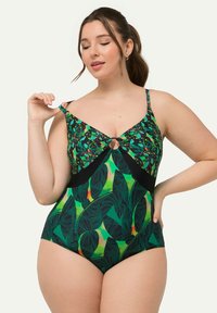 Le maillot de bain une pièce vert présente un motif floral et de feuilles, un accent en forme de trou de serrure à l'avant, des bretelles ajustables et des panneaux latéraux noirs.