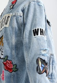 Giacca di jeans, blu chiaro, con ricami di un tigre, rose e una farfalla. Include toppe e dettagli strutturati.