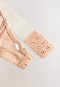 Bežový predlžovač ramienok podprsenky s viacerými háčikmi a očkami na svetlom pozadí, zobrazujúci detaily zapínania.