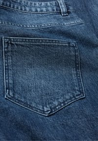 Detailný záber zadného vrecka na modrých džínsach, ktorý zobrazuje textúru látky a detaily stehov.