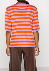 Suéter de manga corta a rayas en naranja y lavanda, con cuello redondo y corte holgado. Tejido de punto texturizado. Pantalones marrones de pierna ancha.