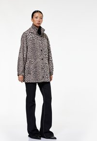 Oversized jas in luipaardprint met een hoge kraag, knopen aan de voorkant en zijzakken; gecombineerd met zwarte flare jeans en zwarte puntige schoenen.