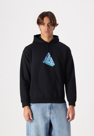 Black hoodie in cotton blend features a front pocket and a colorful triangular logo design. The model wears loose-fitting light blue jeans.