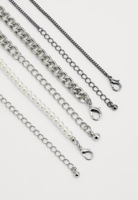 Assorterte kjeder av varierende lengder: sølvfarget metall, svart metall og hvite perler, med hummerlås og ovale lenker.