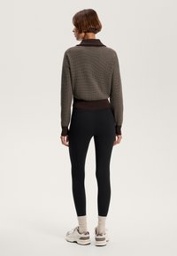 Brown knit sweater with a collar, paired with black high-waisted leggings. Model wears beige sneakers with accents. Smooth texture throughout.