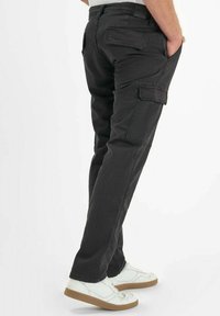 Zwarte cargo broeken met zijzakken, rechte snit en versterkte stitching. Gecombineerd met witte sneakers met rubberen zolen.