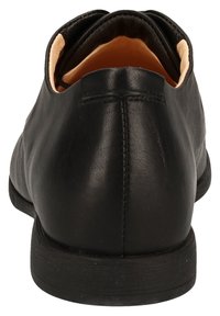 Chaussures en cuir noir avec une texture lisse, un dos arrondi et des détails de couture minimaux. L'intérieur présente une doublure douce de couleur claire.