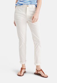 Vita bomullbyxor med rak passform, upprullade benslut och knappstängning. Kompletterade med bruna flip-flops.