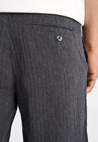 Grå bukser med fiskebensmønster og glat tekstur, som har en sidelomme og en knapdetalje nær taljen.