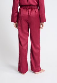 Bordeaux kleurige pyjamabroek met een zachte textuur, voorzien van een gerimpelde tailleband en een klein stippenpatroon. Tapered pasvorm en open zoom.