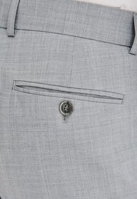 Jasnoszare spodnie z teksturowanej tkaniny, z tylną kieszenią zapinaną na czarny i szary guzik oraz eleganckim, dopasowanym krojem.