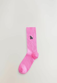 Chaussette de sport rose avec un petit gorille noir brodé près du haut du bord-côte, étendue à plat sur un fond gris clair.