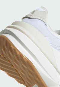 Zapatilla blanca con suela de goma texturizada, parte superior de tela acolchada y un acento gris claro en el talón. Presenta un diseño en capas y acolchado.