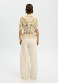 Suéter de punto con mangas cortas, color crema, presenta un patrón de cuadrícula; combinado con pantalones anchos de color beige claro. Textura suave, corte relajado.