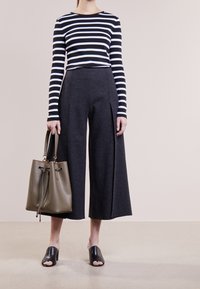 Randig topp med lång ärm i svart och vitt, ihop med vid gråbyxor, hållande en olivgrön bucket bag och bärande svarta öppna klackar.