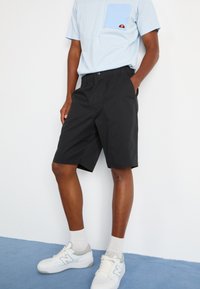 Sorte shorts med elastisk midjebånd, sidelommer, sammen med en lyseblå stripete t-skjorte med brystlomme og logo-detalj.