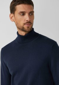 Marineblauer Rollkragenpullover aus glattem Stoff. Er hat eine enganliegende Passform und einen gerippten Kragen, mit minimal sichtbaren Nähten.