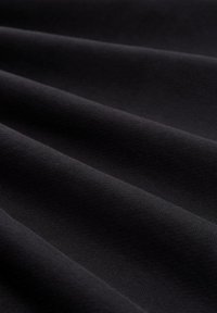 Nærbillede af glat, mørkt stof med diagonale folder, der fremhæver tekstur og subtile lysrefleksioner.